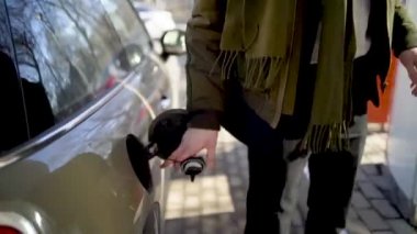 Adam benzin istasyonundaki arabaya hortum sokuyor. Başla. Adam gergin ve hızlı bir şekilde benzin istasyonunda arabaya yakıt dolduruyor. Uzun kovalamaca sırasında araba doldurmak