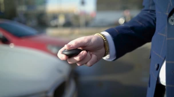 Primer plano del hombre de negocios presionando la llave del coche. Acción. Empresario abre coche con llave electrónica y mira el teléfono. Llave moderna del coche para abrirlo y ponerlo en marcha — Vídeo de stock