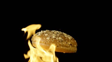 Siyah zemin üzerinde kırmızı alevle izole edilmiş susam tohumlu iştah açıcı bir hamburger ekmeği. Stok görüntüleri. Yemek ve yemek kavramı, alevler içinde dönen çörek..