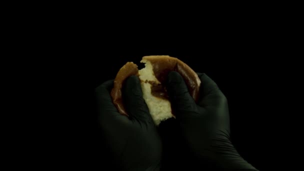Großaufnahme von Bäckermannhänden, die auf schwarzem Hintergrund vereinzelt heißes Brot zerreißen. Archivmaterial. Koch männliche Hände in schwarzen Handschuhen zerreißen kleine Brötchen. — Stockvideo