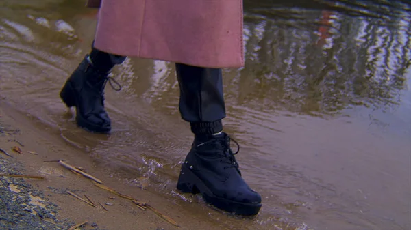 Close up de couro feminino botas pretas andando em uma costa arenosa e da borda da água. Imagens de stock. Detalhes de uma jovem mulher caminhando pelo rio . — Fotografia de Stock