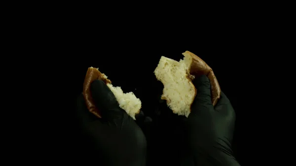 Close-up van bakker man handen scheuren warm brood geïsoleerd op zwarte achtergrond. Voorraadbeelden. Kook mannelijke handen in zwarte handschoenen scheuren kleine broodje. — Stockfoto