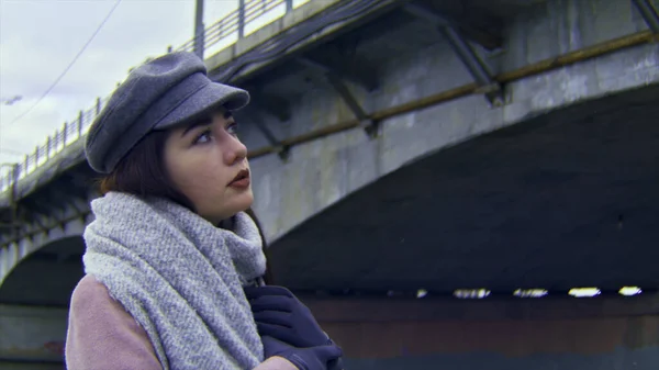 Portrait de jeune femme en manteau rose sur fond de pont et de rivière. Images d'archives. Femme calme et belle portant une casquette chaude et une écharpe triste et coûteuse . — Photo
