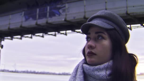 Vista lateral da jovem morena com maquiagem brilhante sob a ponte da cidade. Imagens de stock. Close up retrato de pensativo anf menina triste olhando para longe na beira do rio urbano . — Vídeo de Stock