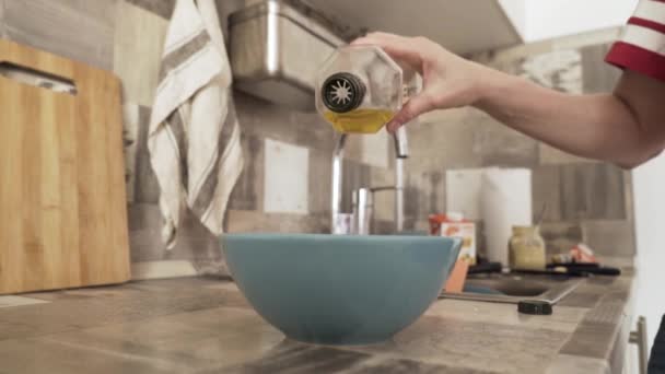 Közelkép nő kezét öntő szűz olívaolaj egy tálba, miközben főzés a konyhában. Felvétel. Nő hozzáadása olaj a mély lemez egy tál, egészséges táplálkozás koncepció. — Stock videók