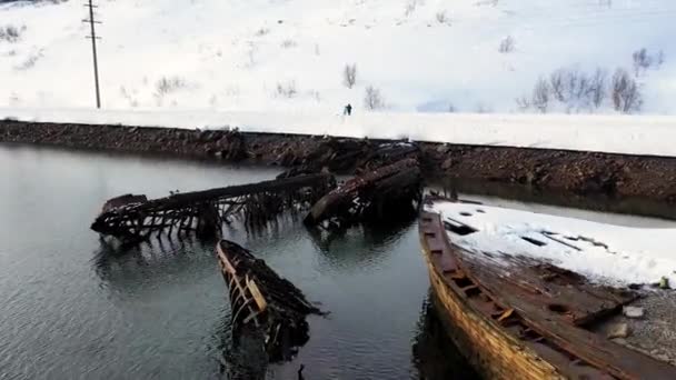 Widok z lotu ptaka na zimowe, śnieżne wybrzeże z zniszczonymi łodziami po katastrofie. Nagranie. Stare zatopione łodzie rybackie na brzegu Morza Barentsa. — Wideo stockowe