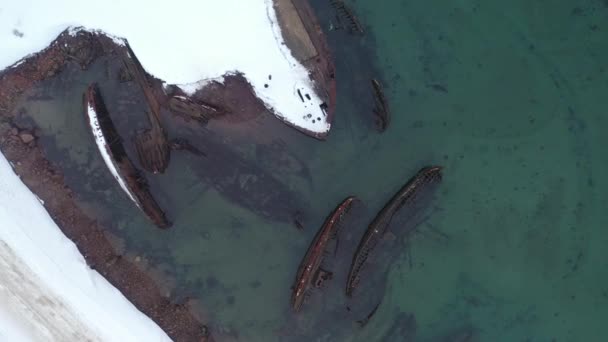 Bovenaanzicht van vele oude wrakschepen verdronken aan de kust in besneeuwde winterseizoen. Beelden. Luchtfoto van de geruïneerde boten in het koude water bij de besneeuwde kust. — Stockvideo