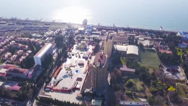 Top uitzicht op huizen en hotels gelegen aan de zeekust. Een knip. Toeristische stad met hotels in de buurt van zeeën rand op zonnige zomerdag. Meerverdiepingen tellende gebouwen met speeltuinen op de achtergrond van de zee — Stockvideo