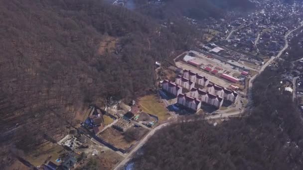 Vista superior de la ciudad situada en el valle del bosque de montaña. Clip. Angosto valle montañoso con laderas boscosas y pequeño pueblo ubicado en él. Pequeña ciudad desarrollada en valle de montaña — Vídeo de stock