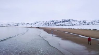 Kışın deniz kıyısında yürüyen gezginler. Görüntü. Kış sahillerinin güzel manzarası, yürüyen insanlar ve kışın karaya oturmuş terk edilmiş eski gemi.