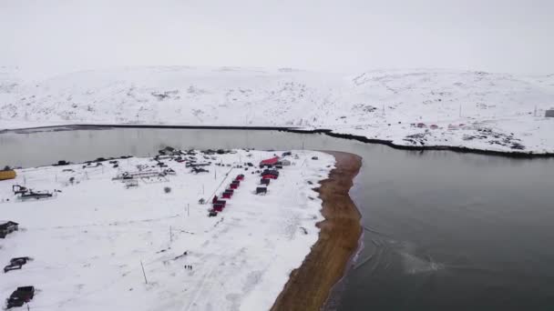 Coastal village by water on background of hills in winter. Footage. Top view of fishing village located on lake shore on background of snowy hills in winter — Stock Video