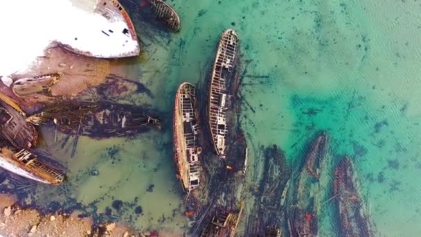 Old sunken ships near coast in winter. Footage. Top view of graveyard of ships in turquoise water off snowy coast in winter. Sunken ships near shore with turquoise winter water — Stock Video
