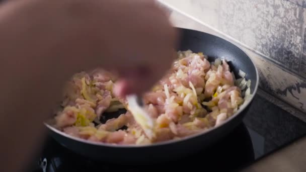 Close-up van roerende stukken vlees met uien in koekenpan. Actie. Rauwe stukjes kipfilet bakken met uien als lunch — Stockvideo