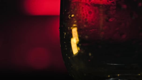 Närbild av isbitar som faller i tomt glas. Lagerbilder. Uppfriskande isbitar faller i transparent glas på mörk neon bakgrund. Cocktailbar — Stockvideo