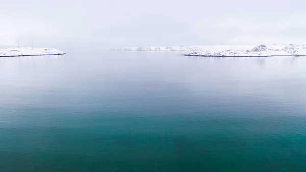 Top view of sea on background of coast in winter. Footage. Beautiful winter panorama of quiet blue sea on background of snowy coast — Stock Photo, Image