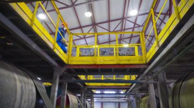İşçi fabrikadaki ekipmanların çalışmasını izliyor. Stok görüntüleri. Çalışan türbinlerin üzerinden geçen işçilerin alt görüntüsü. İşçi monitörleri dönen tanklar