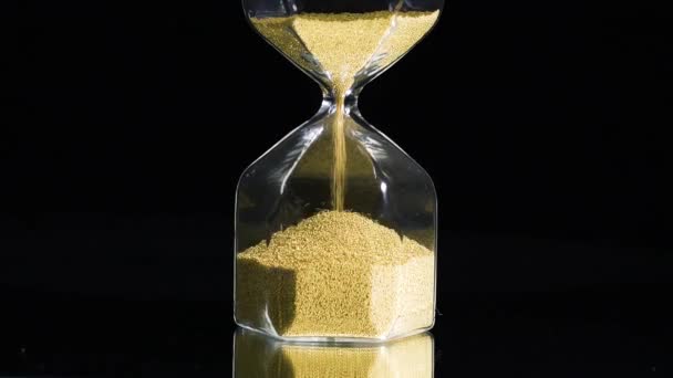 Close-up of Golden hourglass on black background. Stock footage. Golden grains in hourglass had completely crumbled. Golden grains of time in hourglass have run out — Stock Video