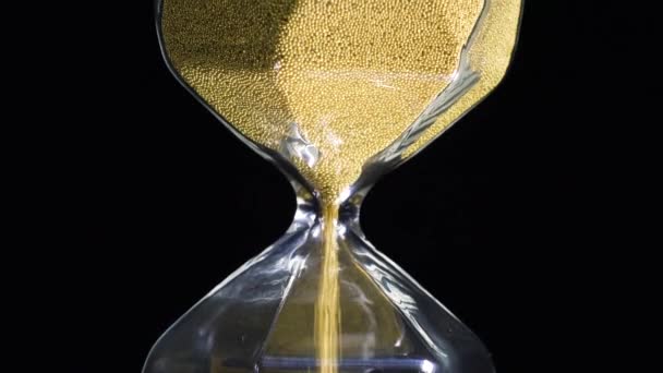 Nahaufnahme einer goldenen Sanduhr. Archivmaterial. Stilvolle Sechseck-Sanduhr mit fallenden Goldflecken auf schwarzem, isoliertem Hintergrund. Der Lauf der Zeit und die Bedeutung jedes Körnchens — Stockvideo