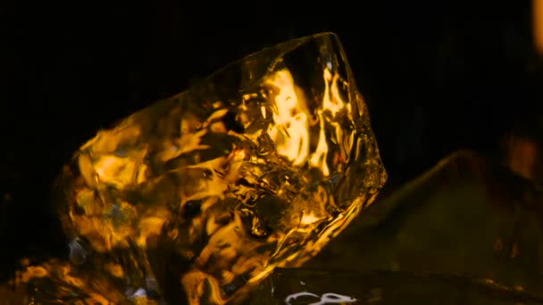 Bebida que se vierte en vidrio transparente con hielo. Imágenes de archivo. Close-up hermosos cubitos de hielo están iluminados con luz de neón y llenos de bebida sobre fondo oscuro — Vídeo de stock