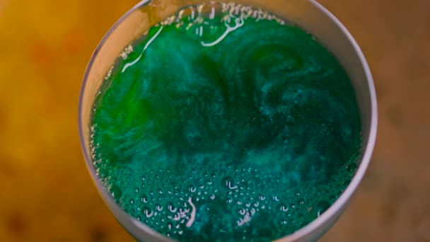 Close-up of beautiful sparkling drink in transparent glass. Stock footage. Luxurious colored drink with bursting bubbles on surface and iridescent sparkling texture — Stock Video