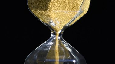 Altın kum saatine yakın çekim. Stok görüntüleri. Siyah izole edilmiş arka planda düşen altın parçacıkları olan stil altıgen kum saati. Zamanın geçişi ve her tahılın önemi