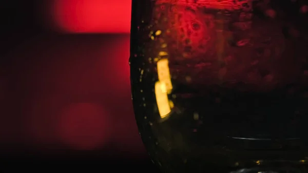 Närbild av isbitar som faller i tomt glas. Lagerbilder. Uppfriskande isbitar faller i transparent glas på mörk neon bakgrund. Cocktailbar — Stockfoto