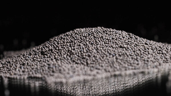 Close-up of gray round grains on black background. Stock footage. Gray round grains for seasoning or decoration on isolated background