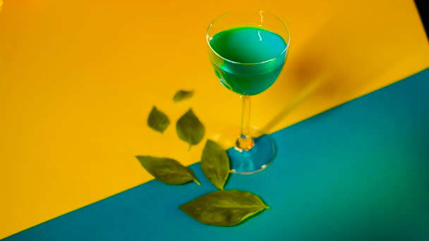 Instelling van alcoholische drank op veelkleurige achtergrond. Voorraadbeelden. Blauwe alcoholische drank staat op decoratieve kleurrijke achtergrond met groene bladeren versieren achtergrond — Stockvideo