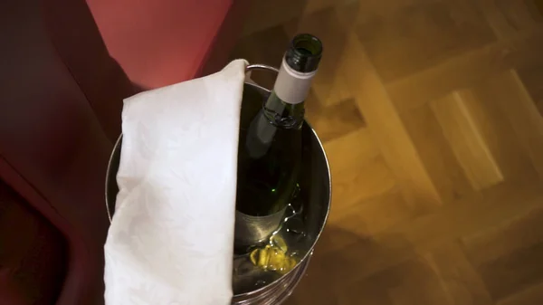 Uma garrafa de champanhe no balde. Imagens de stock. Vista superior do balde de gelo com uma garrafa aberta de bebida alcoólica e pano branco em pé no chão . — Fotografia de Stock