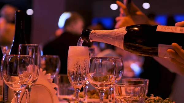 バーやレストランでシャンパンをグラスに注ぐ手の閉じる。ストック映像だ。パーティーでのアルコールの背景、お祝いのコンセプト. — ストック写真