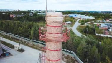 Köyün arka planında tuğla bacası olan bir fabrika. Stok görüntüleri. Yazın yeşil ormanı olan, şehrin arka planında bacası olan tuğla fabrikasının en iyi manzarası.