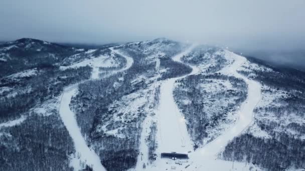 Blick von oben auf das Skigebiet bei bewölktem Wetter. Archivmaterial. Schöne schneebedeckte Berge mit Wäldern und Loipen vor dem Hintergrund von Nebel und bewölktem Winterhimmel — Stockvideo