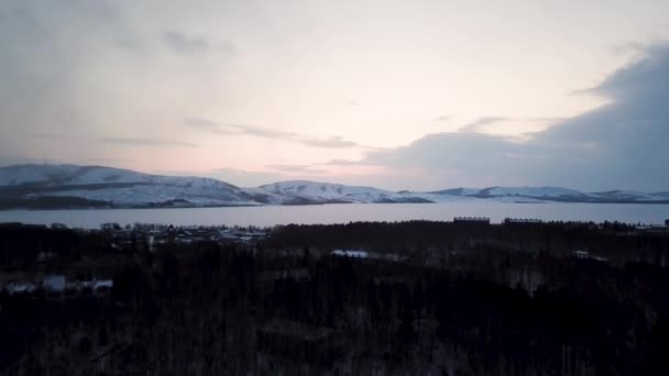 Ovanifrån av vinterlandskap med by vid sjö och skogsklädda kullar. Lagerbilder. Vackert vinterlandskap med skog vid sjö — Stockvideo