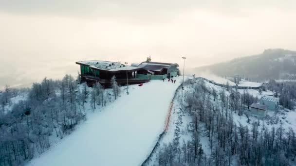 Top view of beautiful landscape from ski resort with track in winter. Stock footage. Top of ski slope with cafe on background of winter cloudy sunset among mountains — Stock Video