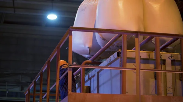 Worker at factory with bags for raw materials. Stock footage. Worker in hard hat opens suspended bags filled with raw materials for mixing in industrial equipment