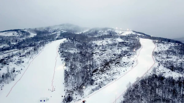 Κάτοψη του χιονοδρομικού κέντρου σε συννεφιασμένο καιρό. Στικ. Όμορφα χιονισμένα βουνά με δάση και μονοπάτια για σκι στο φόντο της ομίχλης και συννεφιασμένο χειμερινό ουρανό — Φωτογραφία Αρχείου