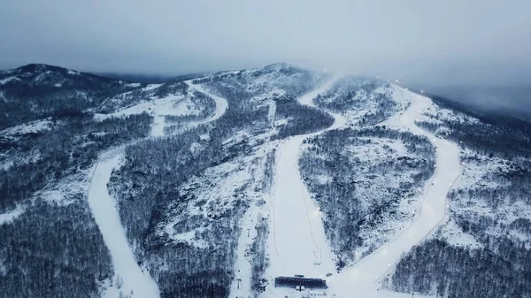 Vista superior da estância de esqui em tempo nublado. Imagens de stock. Belas montanhas nevadas com florestas e trilhas de esqui no fundo do nevoeiro e céu de inverno nublado — Fotografia de Stock
