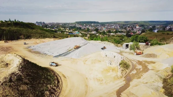 Top view of rubble mining. Stock footage. Mining of rubble or pebbles with heavy transport on background of village in summer