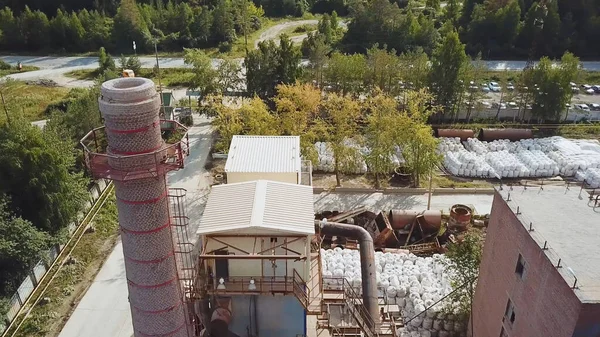 Factory with brick chimney on background of village. Stock footage. Top view of brick factory with chimney on background of town with green forest in summer — Stock Photo, Image