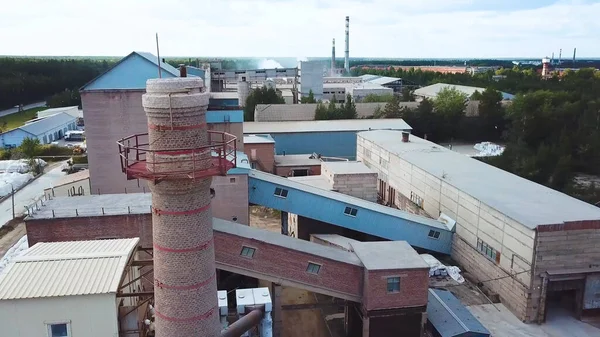 Factory with brick chimney on background of village. Stock footage. Top view of brick factory with chimney on background of town with green forest in summer