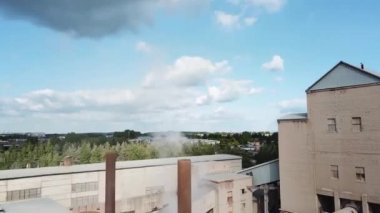 Dumanı tüten küçük bir fabrikanın havadan görünüşü. Stok görüntüleri. Mavi bulutlu arka planda yeşil ağaçlarla çevrili fabrikanın üzerinde uçmak, endüstriyel çalışma kavramı.