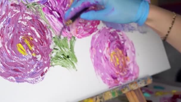 Pintura artística con cuchillo paleta en el taller. Imágenes de archivo. Primer plano de una mujer en gafas pintando hermosas flores rosadas con una herramienta profesional . — Vídeo de stock