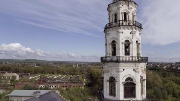 La vieille tour de l'horloge dans la campagne. Images d'archives. Vue aérienne de la tour blanche abandonnée entourée par les maisons de la ville et les arbres verts d'été sur fond de ciel nuageux bleu . — Video
