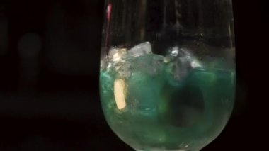 Cam bölmelerinde buz küpleriyle alkolü karıştırmak. Yeşil içecekle şeffaf camları kapatın ve siyah arkaplanda bir kaşıkla karıştırın..