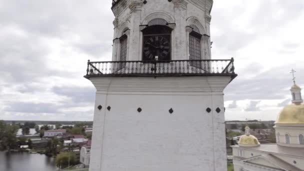 白い古い時計塔の空中ビュー。ストック映像だ。空の背景に都市の建物や緑の木々に囲まれた白い放棄された教会の周りを飛んで、宗教の概念. — ストック動画