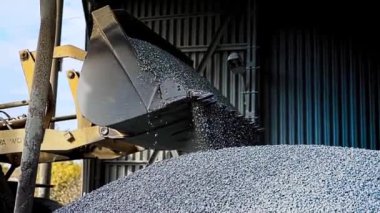 Kazıcının kovayı çakılla çevirdiği yan görüntü. Stok görüntüleri. Profesyonel bir makine, içi tamamen dolu bir kovayla metal hangarı küçük parçalanmış taşlarla dolduruyor..