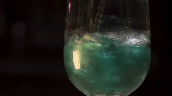 Перемішувати алкоголь з кубиками льоду в склянці Стокові кадри. Крупним планом прозоре скло з зеленим напоєм перемішується з ложкою, ізольованою на чорному фоні . — стокове фото