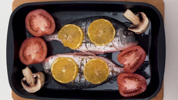 Vista superior del proceso de cocción de pescado. Acción. Primer plano de pescado crudo cortado, salado y picado, hormiga a la parrilla con champiñones, tomates y rodajas de naranja, concepto de comida saludable . — Foto de Stock