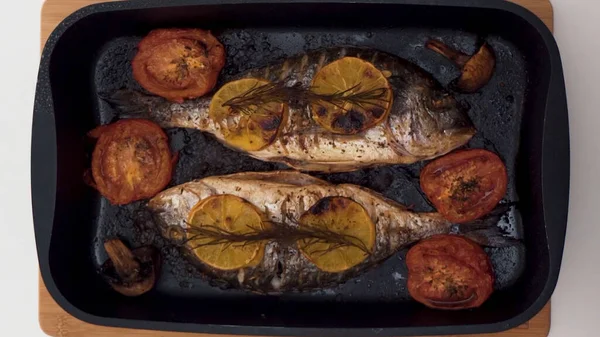 Vista superior del proceso de cocción de pescado. Acción. Primer plano de pescado crudo cortado, salado y picado, hormiga a la parrilla con champiñones, tomates y rodajas de naranja, concepto de comida saludable . — Foto de Stock