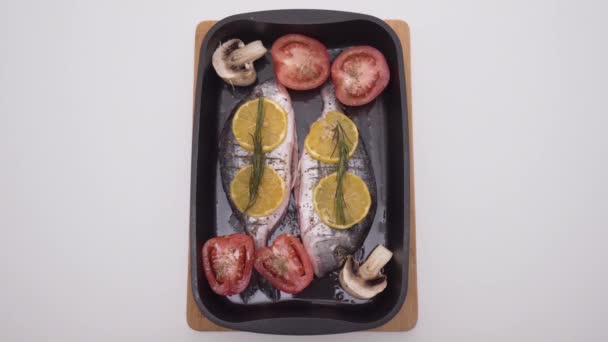 Two raw fish with spices and vegetables in baking tray. Action. Beautiful raw fish with vegetables on baking sheet before baking in oven. Cooking delicious fish in oven — Stock Video